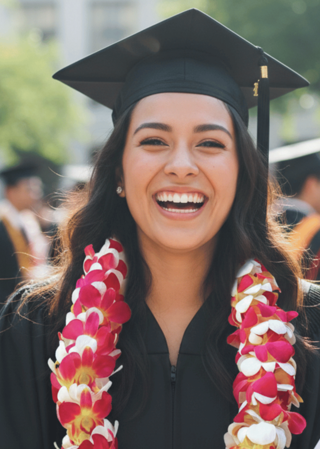 Graduate wearing a black cap and gown with a lei, smiling outdoors.