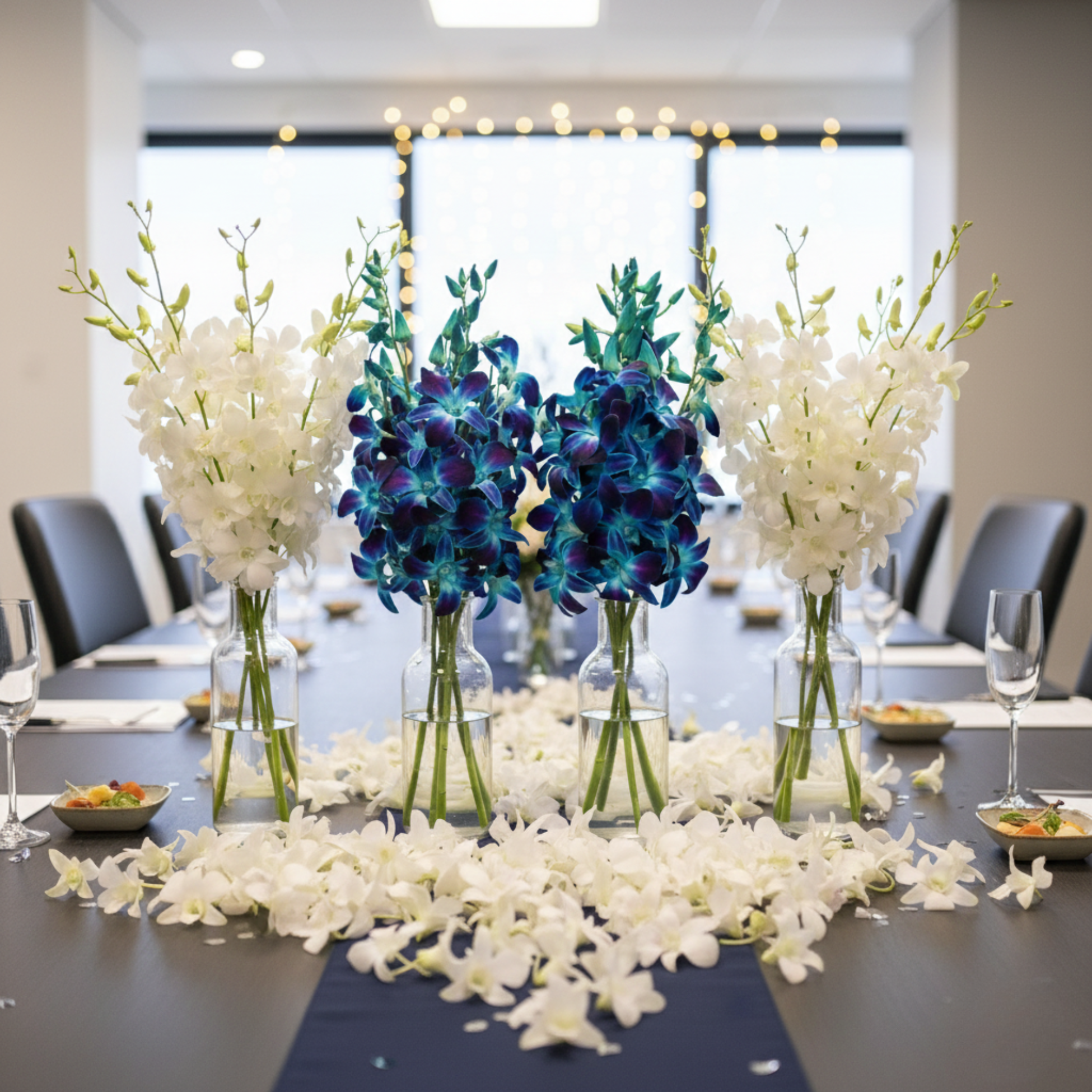 Corporate event table setup with blue and white orchids and scattered white blooms for a modern floral centerpiece.